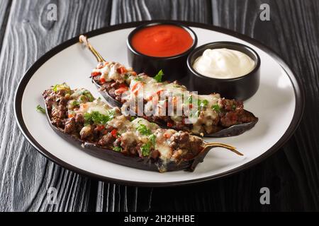 Porzione di melanzana farcita di carne, verdure e cotta con formaggio servito con salse da vicino in un piatto sul tavolo. Orizzontale Foto Stock