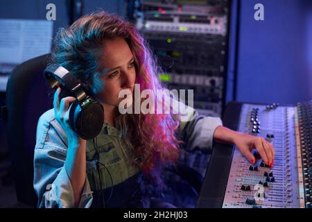 Primo piano di cuffie giovani donne con tastiera elettronica mentre si lavora in studio di registrazione digitale Foto Stock