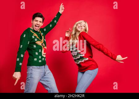 Foto ritratto ridendo coppia indossando maglioni ballando a festa di Natale festeggiamenti isolato vivido rosso sfondo di colore Foto Stock