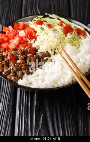 Il piatto Takoraisu è composto da carne macinata, formaggio, lattuga e pomodori serviti su un letto di riso a grani corti primo piano in una ciotola sul tavolo. Verticale Foto Stock