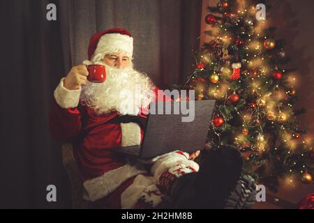 Autentico Babbo Natale sta lavorando su un portatile. Interni domestici. In previsione di Natale e Capodanno. Foto Stock