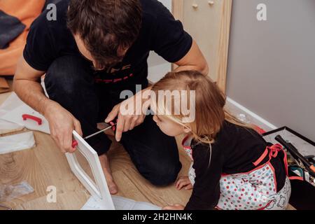 Piccola figlia carina aiuta suo padre fissare mobili in legno. Foto Stock