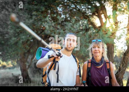 Un paio di escursionisti in mezzo alla foresta che trasportano i loro zaini. L'uomo indica con il suo bastone a piedi il percorso che dovrebbero seguire e il Foto Stock