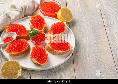 Sandwich con caviale rosso e limone su sfondo beige. Vista laterale, spazio di copia. Foto Stock