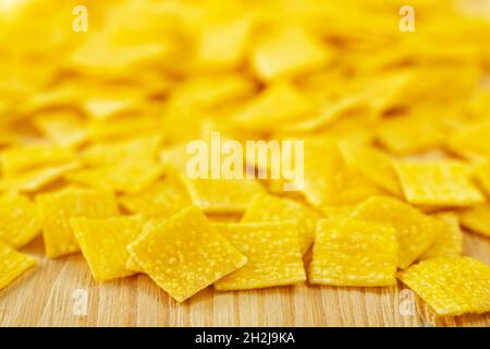 Mucchio di quadretti piatti di pasta all'uovo chiamata quadrucci su fondo legno, pasta di colore giallo con superficie ruvida Foto Stock