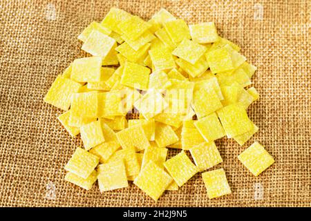 Mucchio di quadretti piatti di pasta all'uovo chiamata quadrucci su fondo di sacco, pasta di colore giallo con superficie ruvida Foto Stock