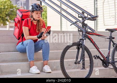 Una ragazza di consegna seduta sulle scale in attesa del prossimo ordine Foto Stock