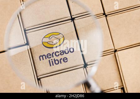 Foto modificata del logo Mercado Libre su una scatola sotto una lente d'ingrandimento circondata da pacchi. Foto Stock