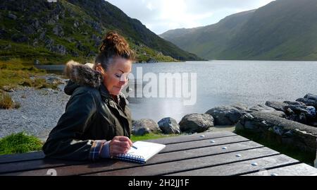 Donna matura che disegna accanto ad un lago irlandese - John Gollop Foto Stock