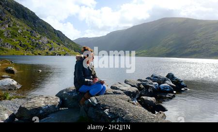 Donna matura che disegna accanto ad un lago irlandese - John Gollop Foto Stock