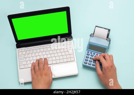 Digitazione manuale su un portatile con uno schermo verde e premendo i pulsanti su un registratore di cassa su sfondo blu, spazio di copia. Il cassiere seleziona l'articolo e. Foto Stock