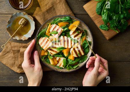 Mangiare insalata sana con pomodori, spinaci, formaggio halloumi, miele. Mani femminili senza volto Foto Stock