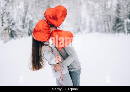 Coppia amorevole coccole nella foresta invernale tenendo palloncini a forma di cuore Foto Stock