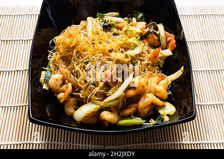 Porzione di Mien Xao vietnamita wok tagliatelle di vetro fritto con verdure e gamberi in ciotola nera da vicino su tavola di legno Foto Stock