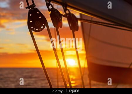 Primo piano di blocchi barca a vela / pulegge a vela silhouetted contro il cielo arancione tramonto sul Mar dei Caraibi Foto Stock