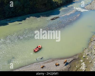 Vista con drone di una barca che naviga lungo un fiume di montagna tra le montagne in una giornata di sole in Georgia Foto Stock