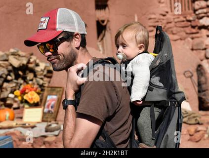 Un uomo porta il suo bambino in uno zaino da trekking, mentre si visita El Rancho de las Golondrinas museo di storia vivente in New Mexico. Foto Stock