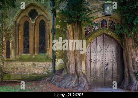 La porta nord della chiesa di St Edward con due antichi alberi di tasso che crescono su entrambi i lati, Stow on the Wold, Gloucestershire. Foto Stock