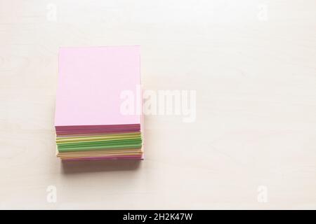 vista dall'alto di pile di fogli colorati bianchi di carta da appunti su un asse di legno marrone chiaro con copyspace Foto Stock