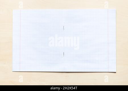 vista dall'alto di un quaderno vuoto aperto con fogli quadrati con margini su asse di legno marrone chiaro Foto Stock