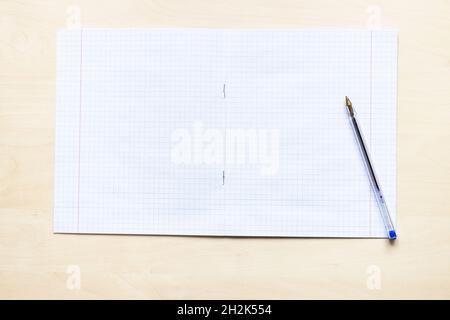 vista dall'alto della penna e del quaderno vuoto aperto della scuola con fogli quadrati con margini su asse di legno marrone chiaro Foto Stock