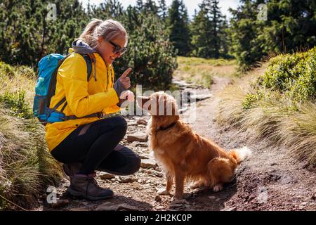 Donna escursioni con il suo cane all'aperto. Nova Scotia Duck Tolling Retriever con proprietario di animali in natura. Donna sorridente che fa l'addestramento di obbedienza al suo dur del cane Foto Stock