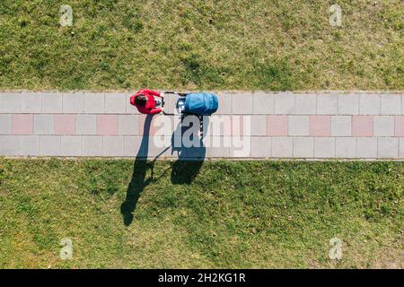 Vista aerea del genitore con un passeggino in una passeggiata durante la giornata di sole, prospettiva direttamente sopra Foto Stock