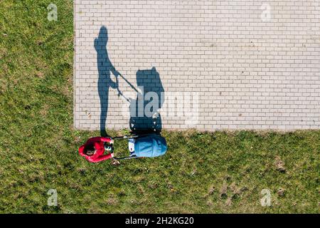 Vista aerea del genitore con un passeggino in una passeggiata durante la giornata di sole, prospettiva direttamente sopra Foto Stock