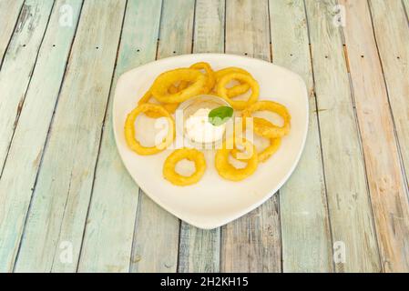 Porzione di anelli di cipolla martellata e fritta in olio d'oliva accompagnata da salsa aioli per l'immersione Foto Stock