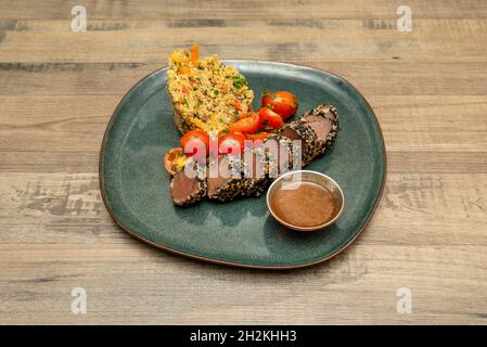 Deliziosa tataki di tonno rosso accompagnata da insalata di pomodoro ciliegia guarnita con olio d'oliva e guranicion di quinoa con verdure e salsa Foto Stock