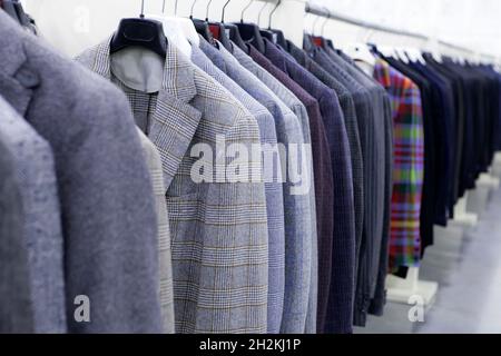 Giacche tweed da uomo in grigio, a scacchi, a righe appendere sugli appendiabiti nel negozio. Stile aziendale Foto Stock