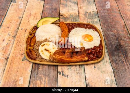 Vassoio popolare colombiano paisa con chorizo, chicharrones, stufato di fagioli rossi, uova fritte, arepa di mais, riso bianco e avocado con plantain fritto Foto Stock