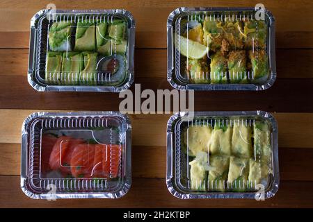 Quattro scatole in plastica per alimenti con sushi e sashimi dall'alto. Servizio di consegna su ordinazione presso il ristorante giapponese Foto Stock