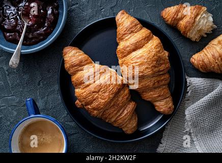 Deliziosi croissant alla burro con marmellata e caffè su sfondo blu. Foto Stock