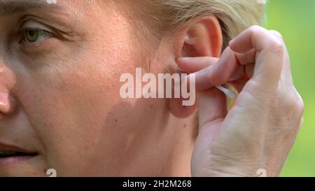 Una ragazza con capelli biondi e un taglio corto pulisce l'orecchio con un bastoncino di cotone primo piano. Foto Stock