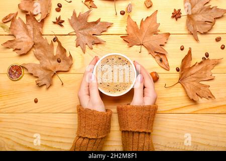 Mani femminili con tazza di caffè e foglie su sfondo di legno Foto Stock