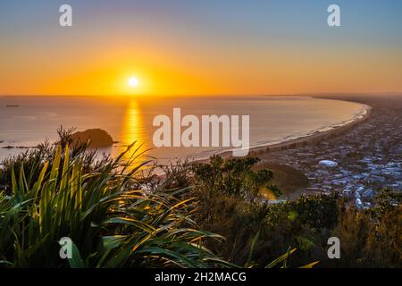 Bagliore d'oro del sole che sorge su un orizzonte lontano con la lunga costa di Bay of Plenty con Leisure Island dalla cima del Monte maunganui. Foto Stock