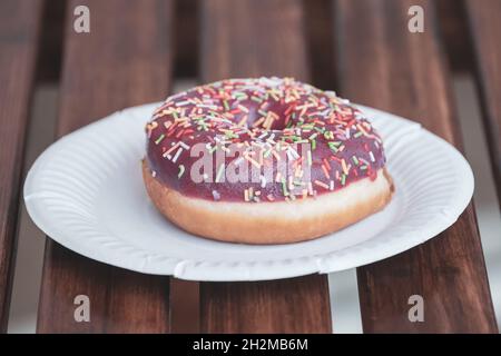 deliziosa ciambella su un piatto di carta bianca su un tavolo di legno di un caffè di strada. Foto Stock