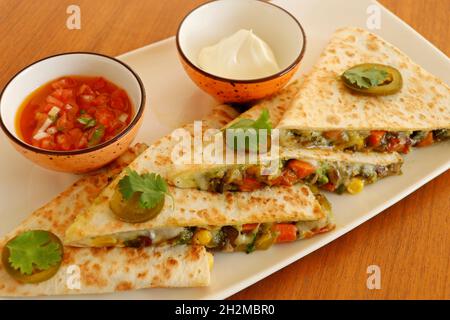 cibo messicano quesadilla, pollo piccante cotto e verdure farcite in tortilla pane con formaggio, guacamole, salsa di pomodoro e panna acida Foto Stock