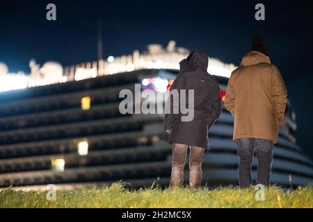 Papenburg, Germania. 23 ottobre 2021. Gli spettatori guardano la nave da crociera di 337 metri 'Aidacosma' che viene trainata attraverso il fiume EMS di notte. Il colosso da crociera di nuova costruzione 'Aidacosmaa' ha iniziato il suo rimorchiatore dal cantiere Meyer sull'EMS al Mare del Nord. Credit: Mohssen Assanimoghaddam/dpa/Alamy Live News Foto Stock