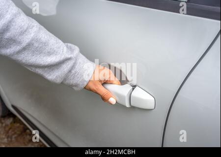 la mano della donna apre la porta bianca dell'automobile. vista parziale della porta dell'automobile di apertura della donna. l'automobile si sblocca. Donna d'affari che apre la porta dell'auto, tiene la maniglia. Primo piano Foto Stock