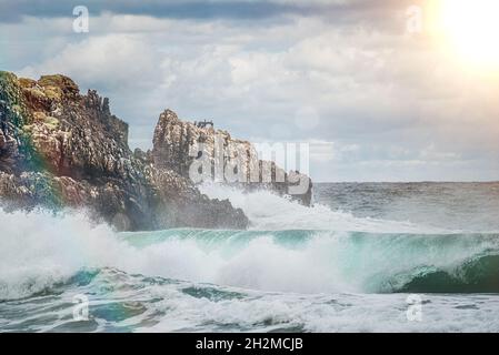 Formazioni rocciose sulla spiaggia contro il cielo. spiaggia con grandi rocce sulla riva e in acqua. Onde potenti sull'oceano. Scogliere frastagliate e mare vorticoso. Robusto, r Foto Stock