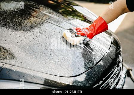 La mano maschio tiene la spugna sopra l'automobile nera per il lavaggio. Foto Stock