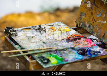 Profondità di campo bassa (fuoco selettivo) immagine con una tavolozza di colori di pittura mentre si dipinge un paesaggio in una soleggiata giornata autunnale. Foto Stock