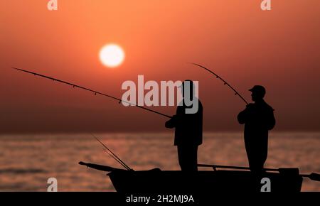 Vecchi amici pesca al tramonto sul mare. Due uomini pescatori silhouette pesca insieme su una piccola barca. Vita semplice e felice Foto Stock