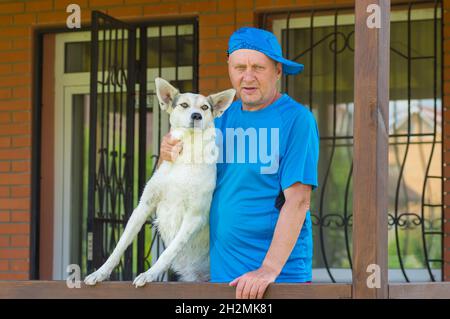 Bel ritratto all'aperto di uomo anziano caucasico e il suo bel cane giovane bianco di razza mista in piedi su una veranda Foto Stock