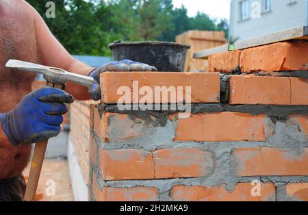 Muratore con martello per muratore per costruire una nuova parete di mattoni rossi all'aperto. Mattoni Basics tecniche di muratura. Foto Stock