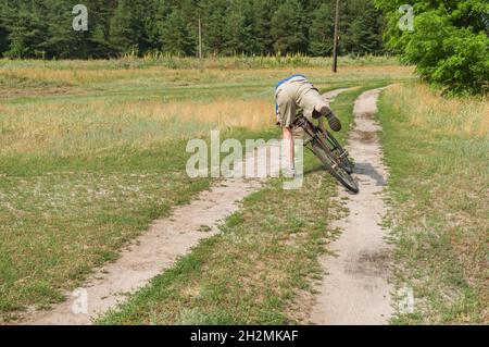Uomo maturo che cade da un'antica bicicletta su una strada di campagna nel villaggio rurale in Ucraina centrale Foto Stock