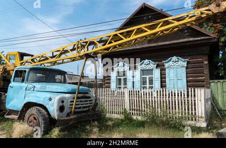 Vecchio camion di gru sovietico arrugginito lasciato di fronte a una casa di legno tradizionale nel villaggio di Barguzin. Repubblica di Buryatia, Russia Foto Stock