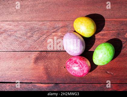 Quattro luminose uova di pasqua multicolore adagiate sul ponte di legno rosso illuminato al sole Foto Stock